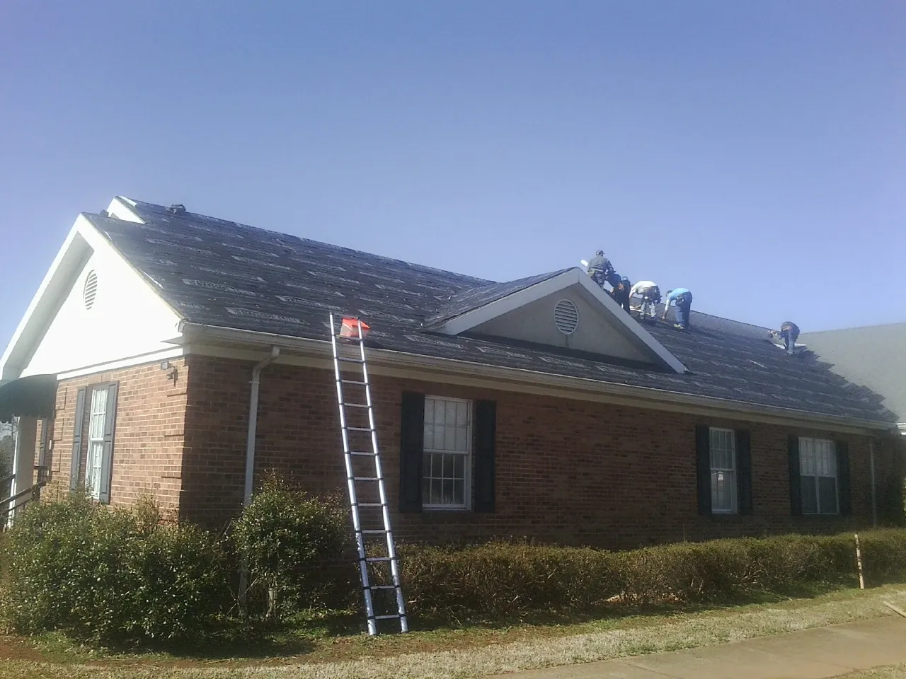 Crew tearing shingles off a brick ranch roof with a ladder set — Emergency Roof Repair work by our crew in Peabody